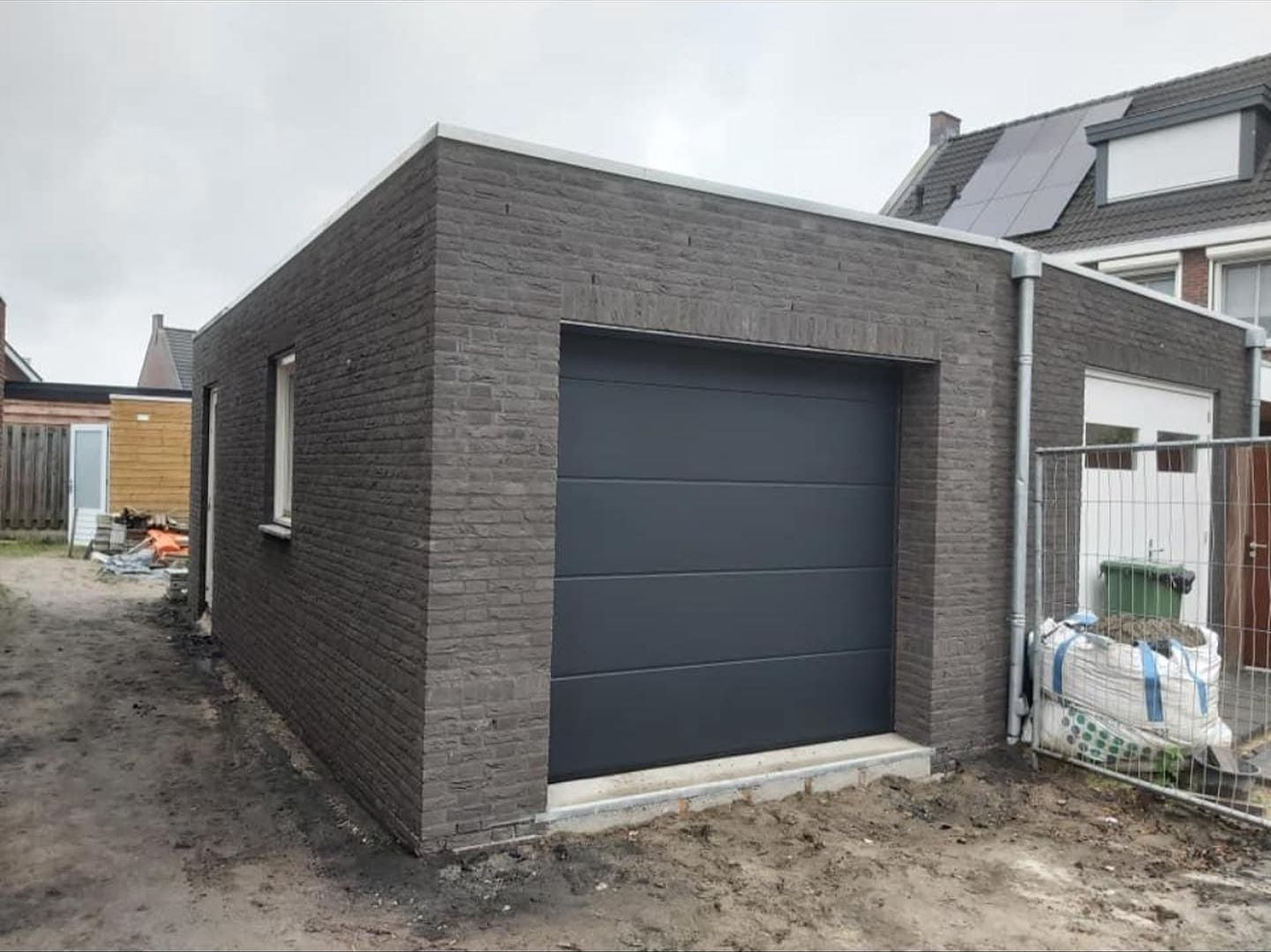 Gemetselde garage in donkere steen met een grijze sectionaaldeur, binnen en buiten schoonwerk